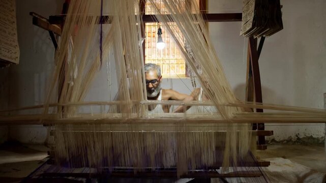 Elderly Indian man weaving on a traditional handloom in a village workshop, working with silk threads to craft handmade fabric