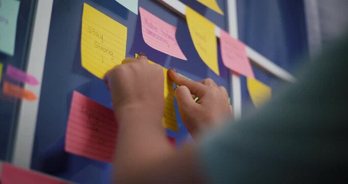 Handheld low angle view shot, Woman's hand sticking a note with a message on a glass window in home office. Ideas and inspiration.