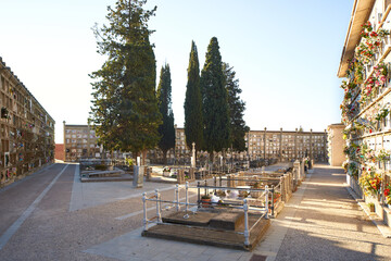View of a Christian cemetery square during the day with niches on the sides and tombs with cypress trees in the center with the sun