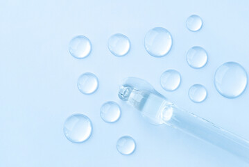 Drop of cosmetics and a pipette on a blue background. A product for skin, face or hair care.