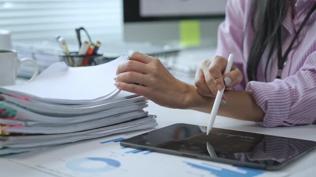 Professional businesswoman reviewing documents, using tablet with stylus, analyzing charts and graphs while working at office desk with focused concentration - Powered by Adobe