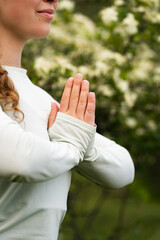 Meditation in nature. Smiling woman meditating with green and white blurry background, holding her hands in namaste gesture, wearing long sleeve, close-up outdoor yoga activities in springtime