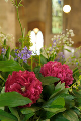 Floral arrangement of pink peonies and wildflowers placed inside a church with soft natural light