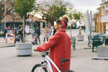 Outdoor fashion portrait of pretty african woman walking with bicycle , wearing long red coat