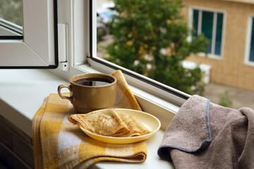 Breakfast against the backdrop of a city street. Breakfast on the balcony against the backdrop of house windows. Pancakes with coffee or tea on the windowsill create coziness.