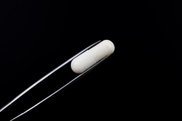 Pliers holding a pill of gut analgesic or anti-inflammatory on black background	