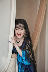 Beautiful gothic vampire woman wearing medieval dress screams and stands among ancient ruin