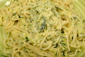 A close-up view presents a vibrant green plate filled with spaghetti and zucchini in a rich, creamy sauce