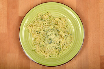 A top-down view shows a plate of spaghetti with zucchini in a creamy sauce, ready to be enjoyed