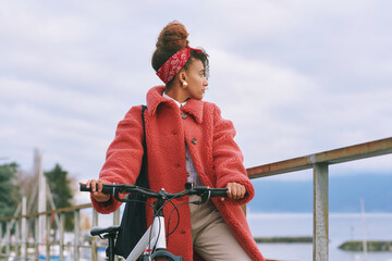 Outdoor fashion portrait of pretty african woman walking with bicycle , wearing red coat
