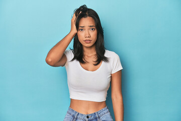 Filipina young woman on blue studio tired and very sleepy keeping hand on head.