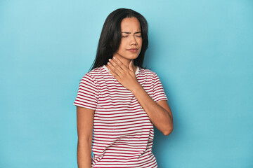 Filipina young woman on blue studio suffers pain in throat due a virus or infection.