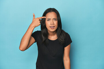 Filipina young woman on blue studio showing a disappointment gesture with forefinger.