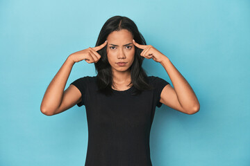 Filipina young woman on blue studio focused on a task, keeping forefingers pointing head.