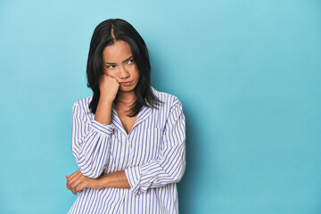 Filipina young woman on blue studio who feels sad and pensive, looking at copy space.