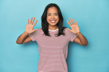 Filipina young woman on blue studio showing number ten with hands.
