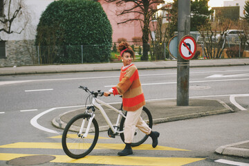 Outdoor portrait of pretty African woman walking with bicycle, crossing crosswalk