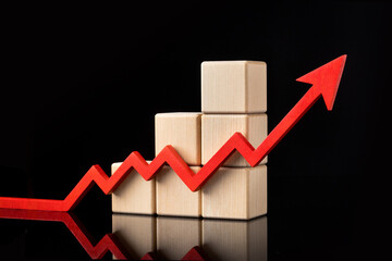 A red upward zigzag arrow next to stacked wooden cubes on a black background with reflection. . High quality photo