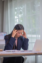 Exhausted businesswoman sitting at desk in office surrounded by documents and charts, facing...