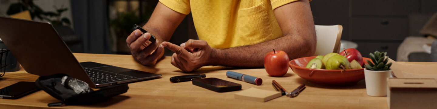 Man checking blood sugar level with glucose meter at home table
