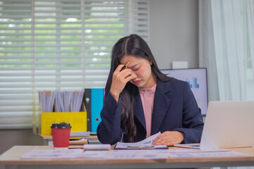 Exhausted businesswoman sitting at desk in office surrounded by documents and charts, facing...