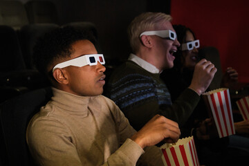 Group of friends wearing 3d glasses watching a movie at the cinema and eating popcorn