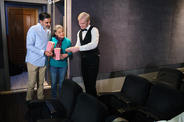 Couple entering movie theater and usher checking tickets, holding popcorn buckets