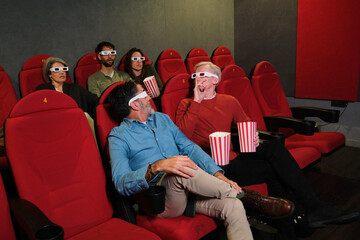 A man turns around in his seat and gestures for silence, politely asking the group behind him to stop talking during the movie