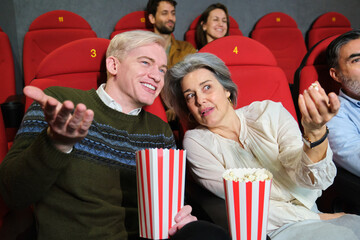 Mature couple enjoying a movie at the cinema, eating popcorn and sharing their impressions