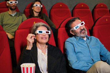 Group of people wearing 3d glasses watching a movie at the cinema, eating popcorn and enjoying the show