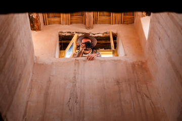 Male photographer in hat taking photo through window of historic building