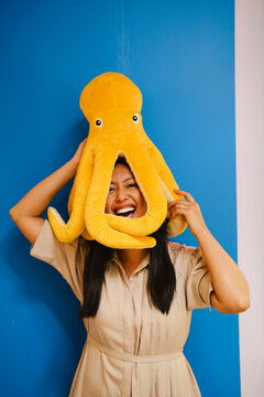 Smiling woman posing with octopus toy on head against blue background