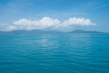 The blue sea and the background have a mountain, clouds, and clear blue sky. 