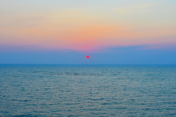 The calm blue sea and sunset view, the sky is turning from blue to orange, and the sun is red. 