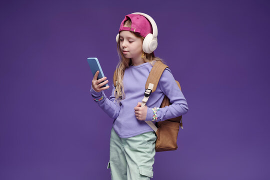 Schoolgirl with headphones and smartphone against purple background