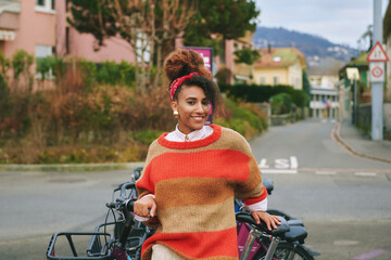 Outdoor fashion portrait of pretty african woman leaning on the bike