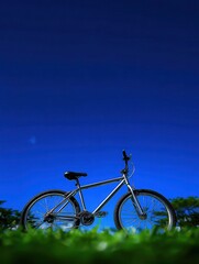 Fototapeta premium A silver bike resting on vibrant green grass under a clear blue sky, This image can symbolize freedom, outdoor adventure, or fitness, making it perfect for travel blogs or fitness articles,