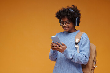 Schoolboy with headphones and smartphone indoors in front of orange background