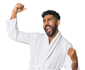 Hispanic male in a robe in studio raising fist after a victory, winner concept.