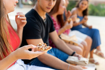 Group of young adults eating pizza and socializing outdoors