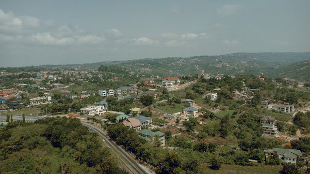 Aerial view of homes nestled among verdant trees and rolling hills under a muted sky, contrasting with the architectural details of the town, Aburi, Eastern Region, Ghana.