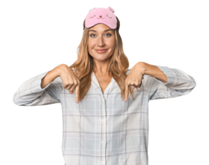 Blonde in pajamas with sleep mask points down with fingers, positive feeling.