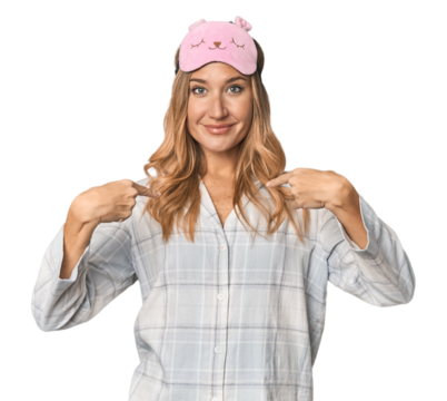Blonde in pajamas with sleep mask surprised pointing with finger, smiling broadly.