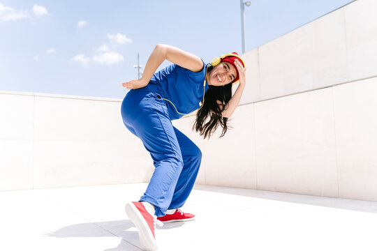Woman doing hip hop dance pose outdoors in blue outfit with red hat