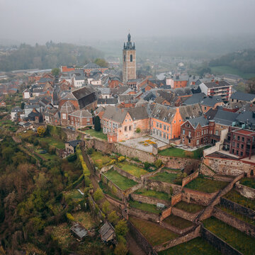 Aerial view of the belfry rising above the historic town nestled on terraced slopes, a tapestry of earth tones against the muted sky, Thuin, Wallonia, Belgium.