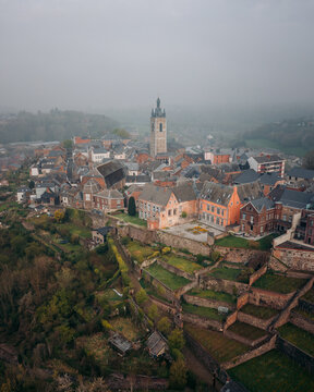 Aerial view of the belfry tower rising above the medieval architecture and terraced gardens under a misty sky, Thuin, Wallonia, Belgium.