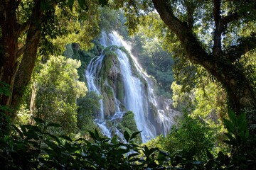 Lush waterfall cascading down rocky cliff face, framed by dense tropical foliage