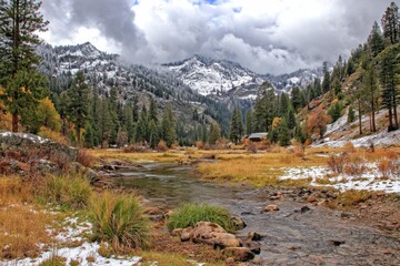 Mountain valley scene with snow-capped peaks, colorful fall foliage, and a meandering river