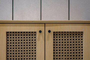 Close-up of modern wooden cabinet doors with natural rattan cane webbing panels and black knobs....