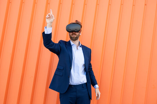 Businessman in suit using VR glasses gesturing against orange background